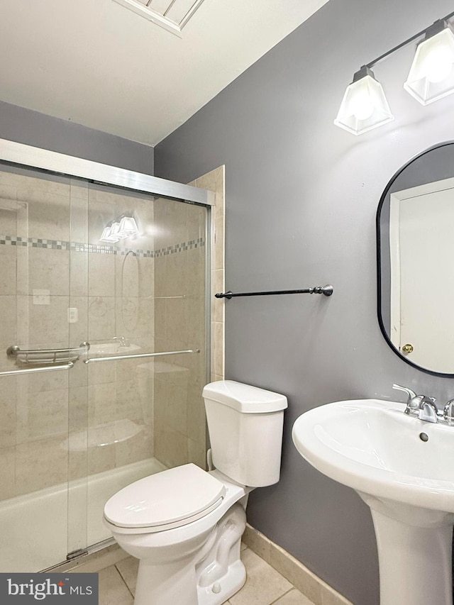 bathroom with toilet, a stall shower, a sink, tile patterned flooring, and baseboards