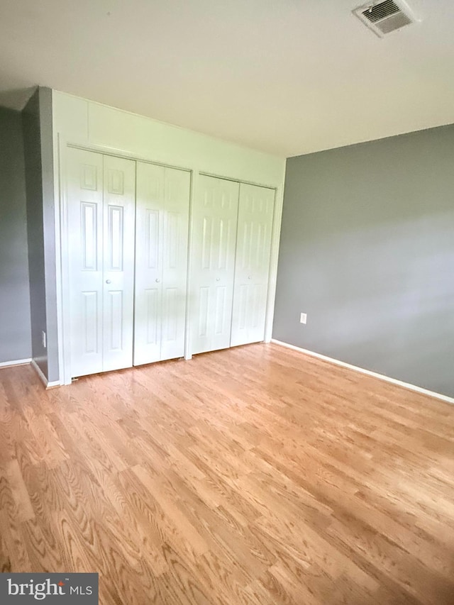 unfurnished bedroom featuring baseboards, visible vents, two closets, and wood finished floors