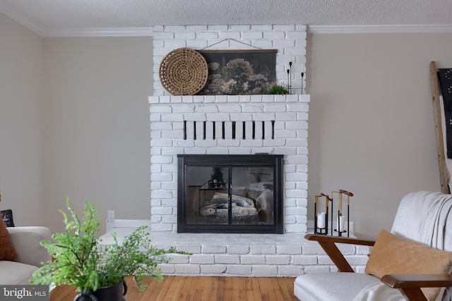 living room featuring wood finished floors, a textured ceiling, a brick fireplace, and ornamental molding