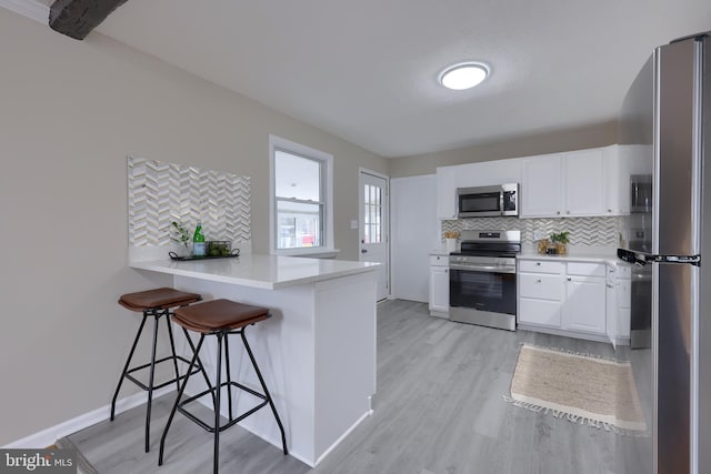 kitchen featuring a breakfast bar, a peninsula, light wood-style floors, appliances with stainless steel finishes, and backsplash