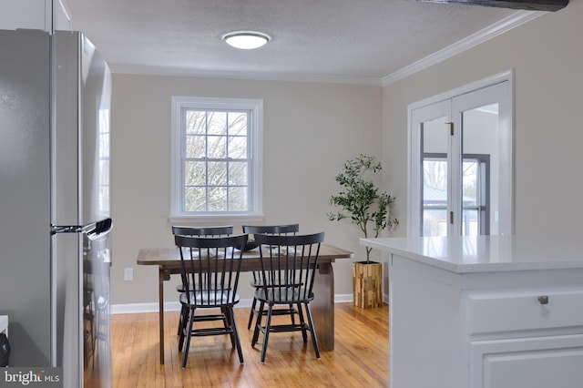 dining space with light wood-style flooring, a textured ceiling, crown molding, and baseboards