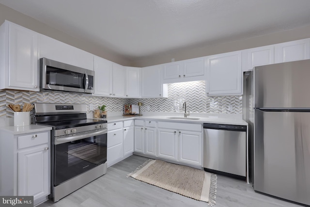 kitchen featuring light wood finished floors, a sink, light countertops, white cabinets, and appliances with stainless steel finishes