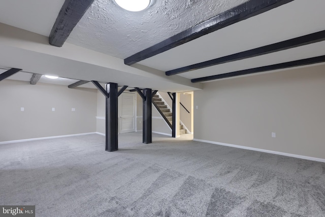 finished below grade area featuring baseboards, a textured ceiling, carpet floors, and stairs