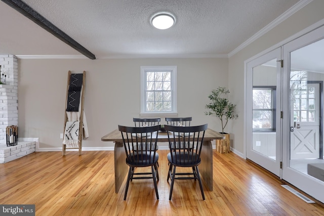 dining area featuring baseboards, a textured ceiling, light wood-style floors, and ornamental molding