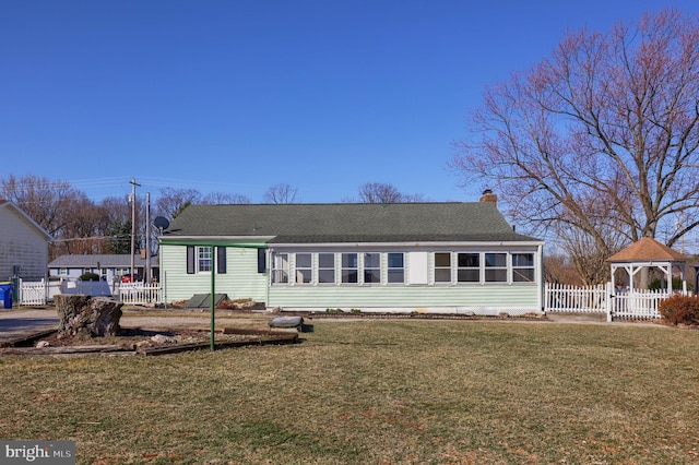 rear view of house featuring fence, a sunroom, a chimney, a gazebo, and a lawn