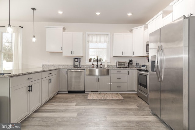 kitchen featuring stainless steel appliances, a peninsula, a sink, white cabinets, and hanging light fixtures