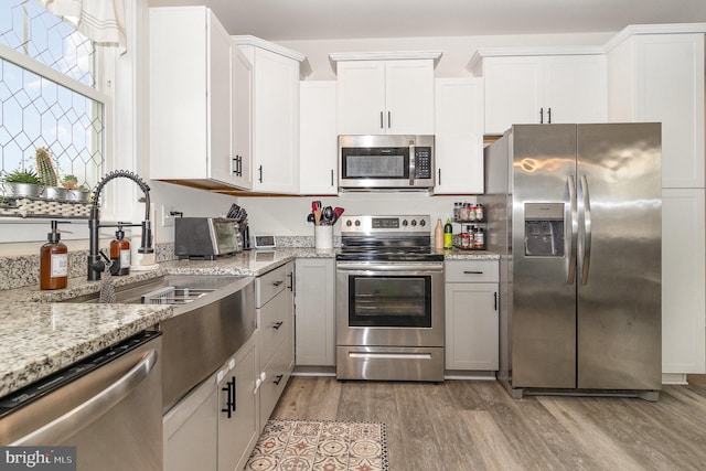 kitchen featuring light stone counters, dark wood-style flooring, stainless steel appliances, white cabinetry, and a sink