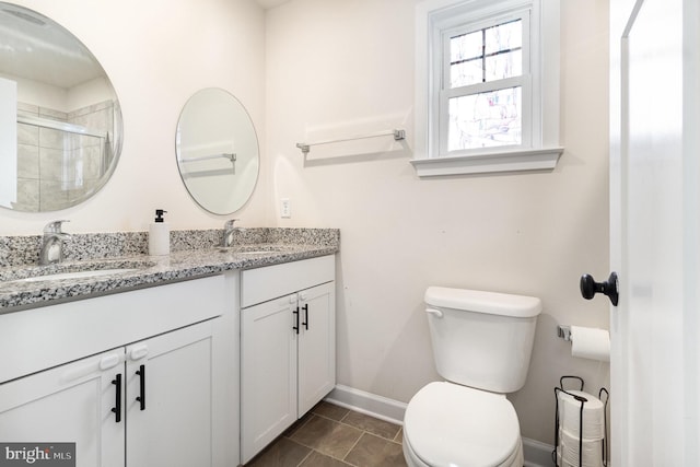 bathroom featuring a tile shower, double vanity, a sink, and toilet