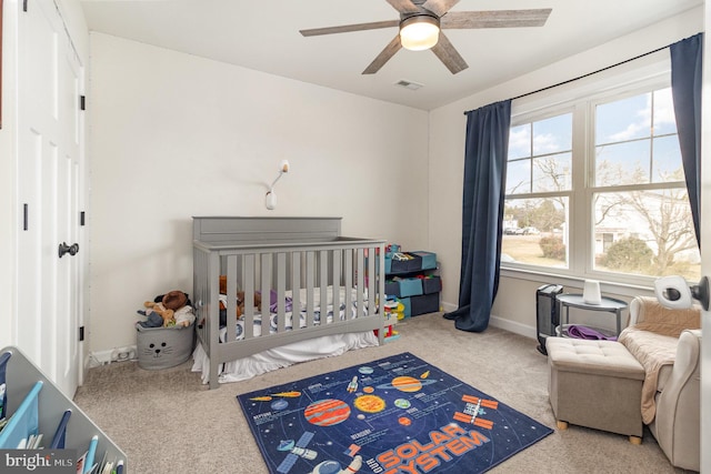 bedroom with a crib, baseboards, visible vents, and ceiling fan