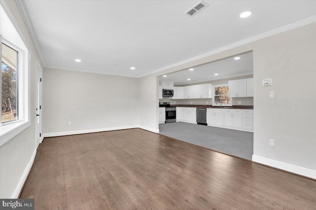 unfurnished living room with baseboards, wood finished floors, visible vents, and crown molding