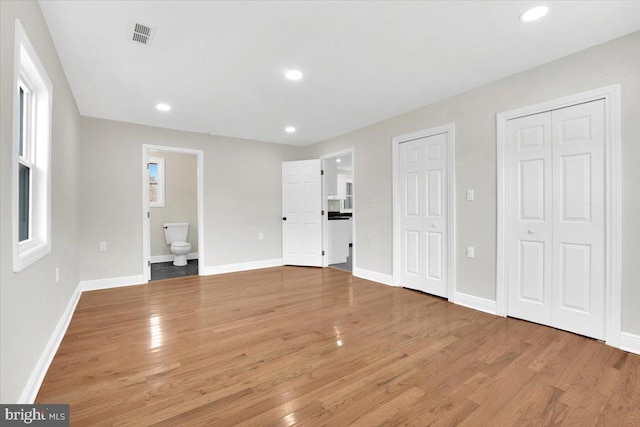 unfurnished bedroom featuring baseboards, two closets, light wood-style flooring, and recessed lighting