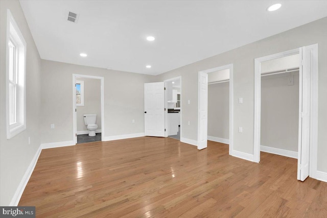 unfurnished bedroom with two closets, recessed lighting, light wood-style floors, ensuite bath, and baseboards