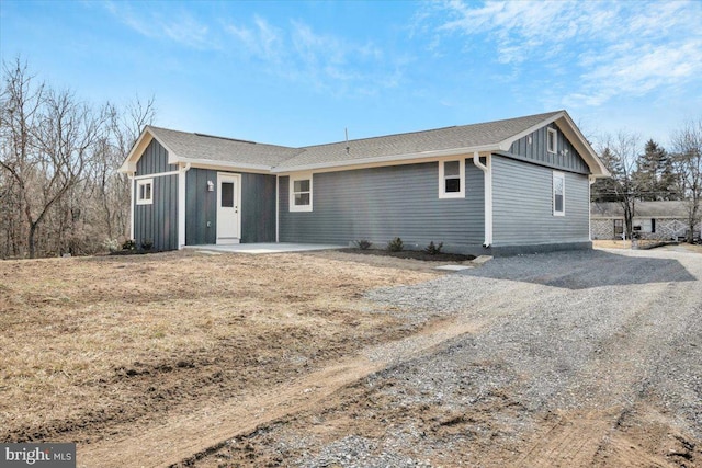 view of front of home with board and batten siding, gravel driveway, and a patio area