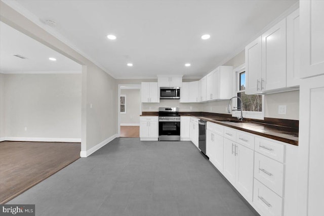 kitchen featuring a sink, baseboards, appliances with stainless steel finishes, dark countertops, and crown molding