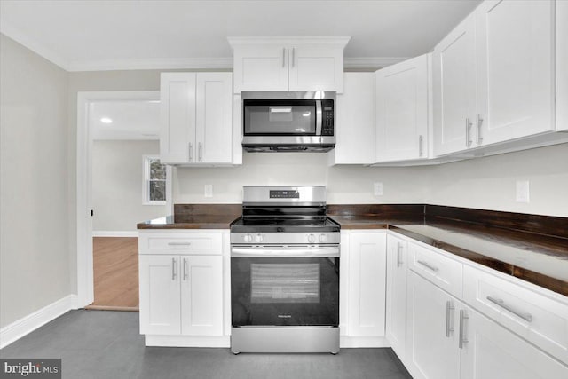 kitchen with appliances with stainless steel finishes, white cabinetry, crown molding, and baseboards