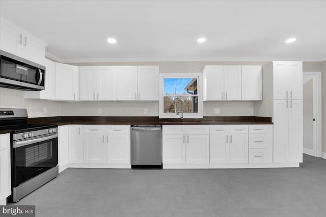 kitchen featuring a sink, white cabinets, ornamental molding, appliances with stainless steel finishes, and dark countertops