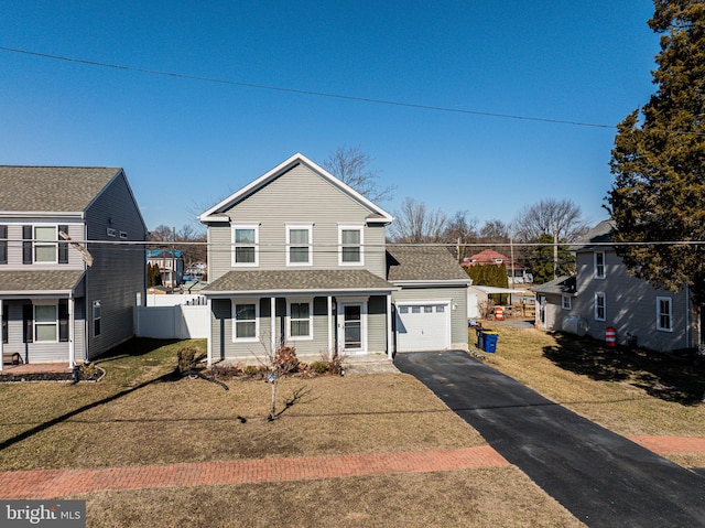 traditional-style home featuring a garage, aphalt driveway, roof with shingles, fence, and a front yard