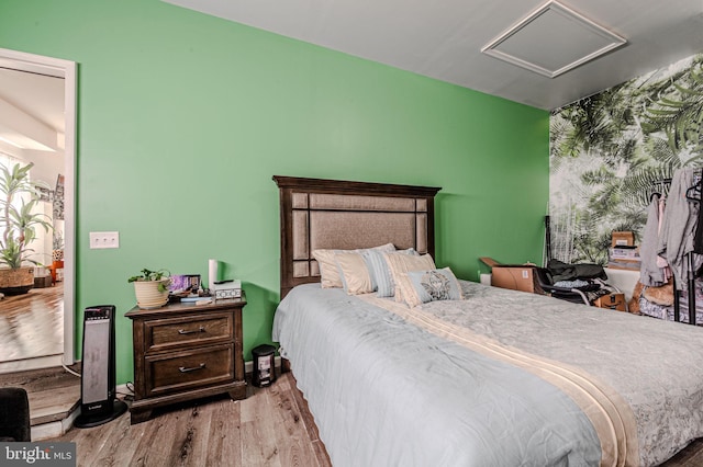 bedroom with an accent wall, wood finished floors, attic access, and baseboards