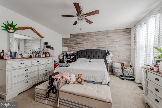 bedroom with an accent wall, light carpet, and a ceiling fan