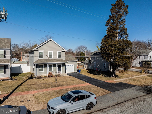 traditional home featuring a garage, fence, driveway, roof with shingles, and a front lawn