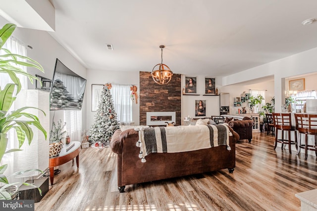 living room featuring a large fireplace, wood finished floors, visible vents, and an inviting chandelier