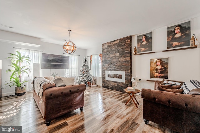 living room with visible vents, a notable chandelier, a stone fireplace, and wood finished floors