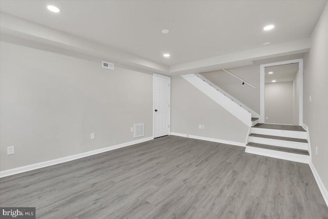 finished below grade area featuring stairs, recessed lighting, visible vents, and wood finished floors