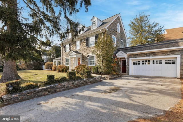 view of front facade featuring stone siding, a front yard, concrete driveway, and a garage