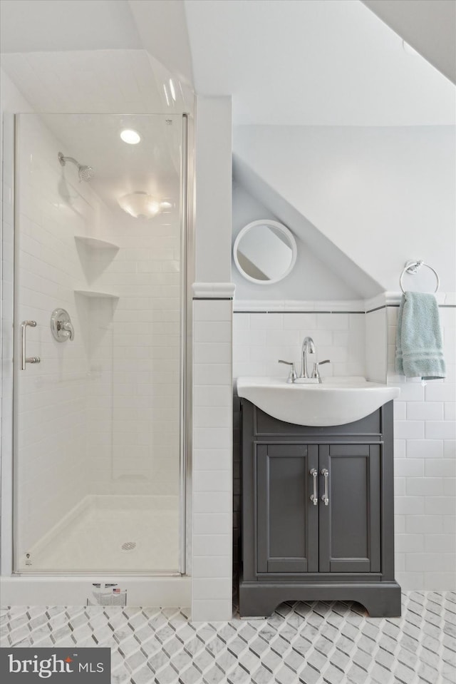 full bath featuring a stall shower, wainscoting, vanity, and tile walls