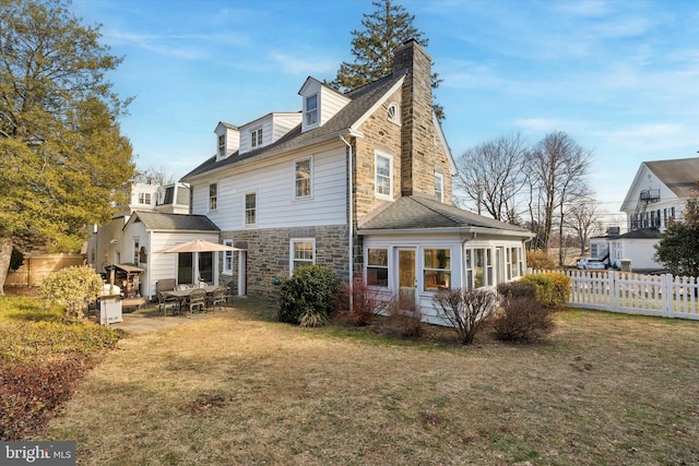 rear view of property featuring a yard, stone siding, fence, and a chimney