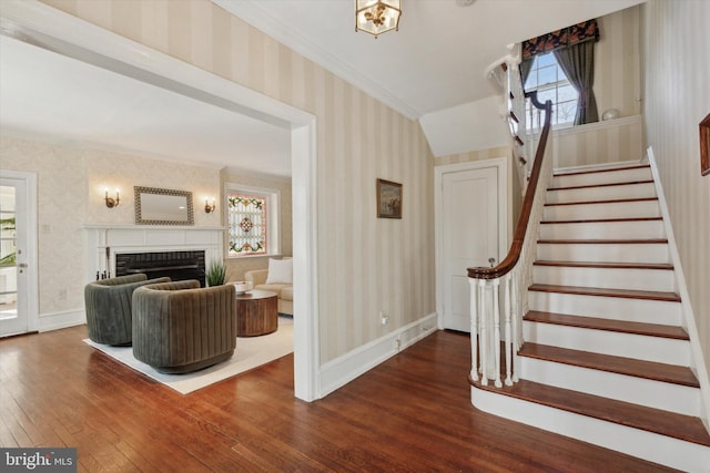 interior space with a fireplace, wood finished floors, baseboards, ornamental molding, and wallpapered walls