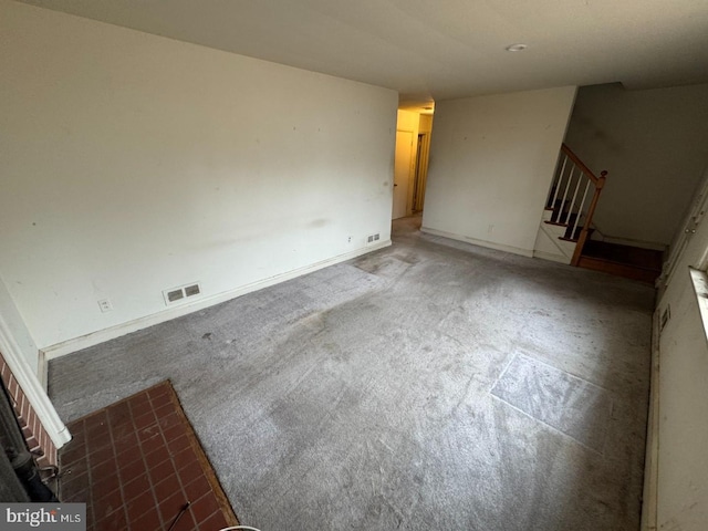 carpeted spare room featuring stairway, visible vents, and baseboards