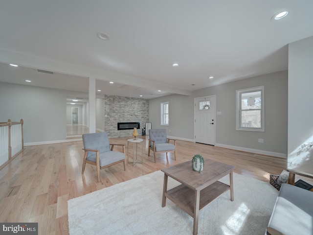 living room with visible vents, baseboards, a stone fireplace, recessed lighting, and light wood-style floors