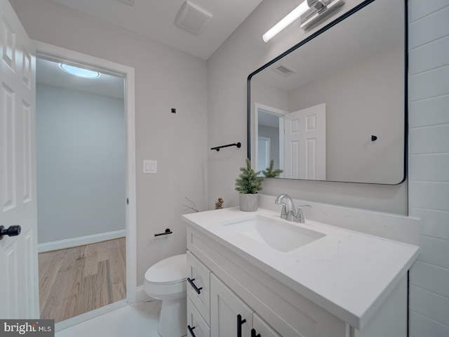 bathroom featuring visible vents, baseboards, toilet, wood finished floors, and vanity