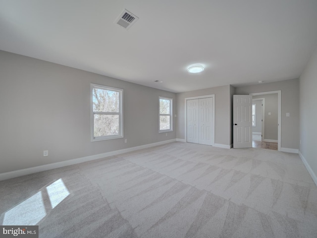 unfurnished bedroom featuring a closet, visible vents, light colored carpet, and baseboards