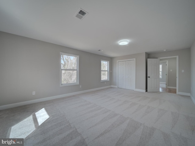 unfurnished bedroom with light colored carpet, baseboards, visible vents, and a closet