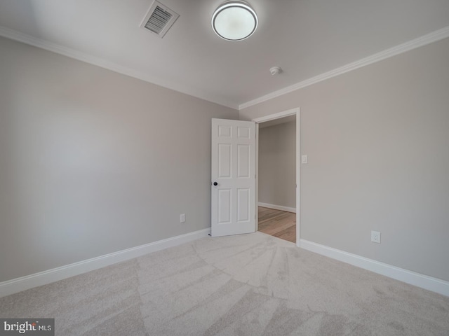 empty room with crown molding, carpet flooring, baseboards, and visible vents