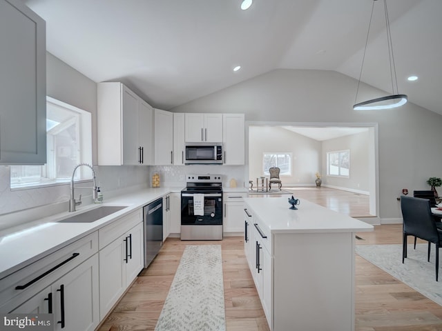 kitchen with light wood finished floors, a kitchen island, a sink, vaulted ceiling, and appliances with stainless steel finishes