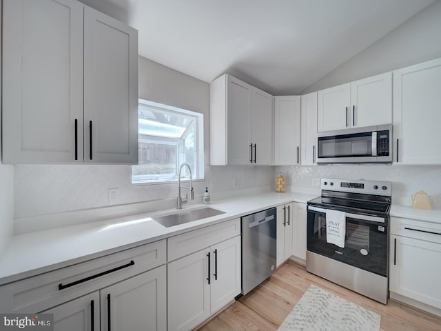 kitchen featuring a sink, appliances with stainless steel finishes, light countertops, decorative backsplash, and lofted ceiling