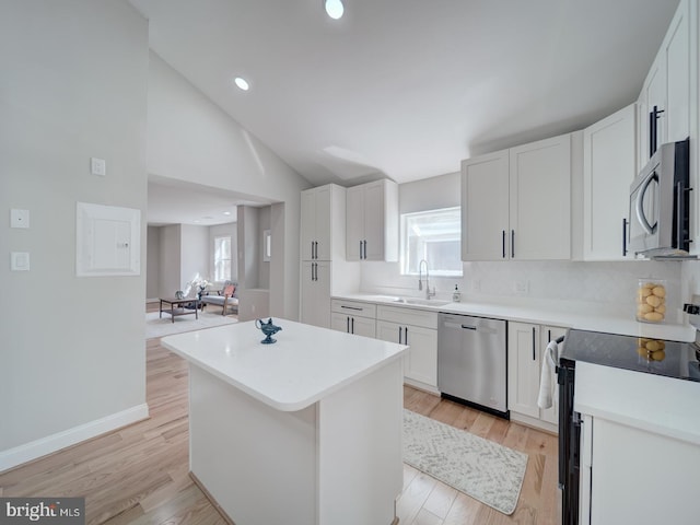 kitchen with a kitchen island, light wood-type flooring, appliances with stainless steel finishes, white cabinetry, and a sink