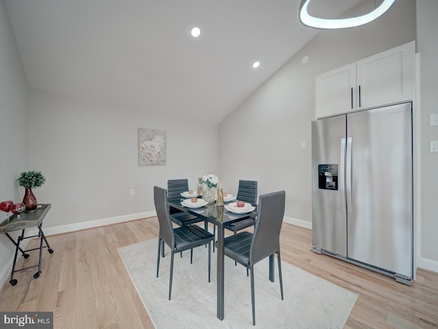 dining space with baseboards, light wood-type flooring, and lofted ceiling