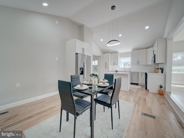 dining room featuring visible vents, light wood-type flooring, and vaulted ceiling