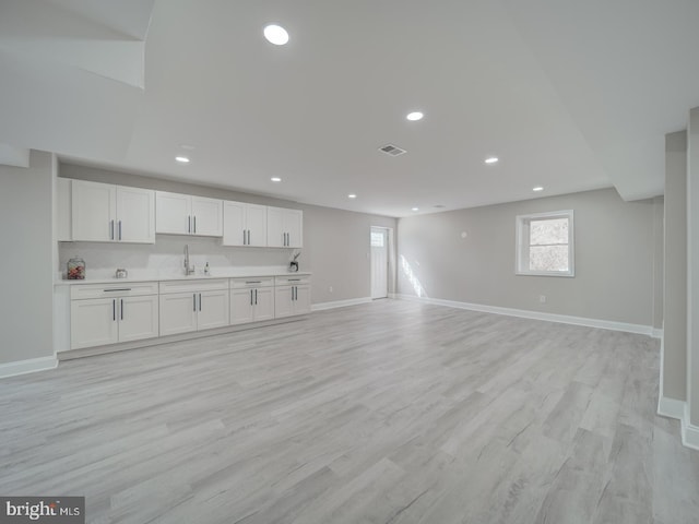 unfurnished living room featuring visible vents, light wood-type flooring, baseboards, and a sink