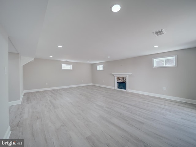 basement featuring light wood finished floors, visible vents, a fireplace, and baseboards