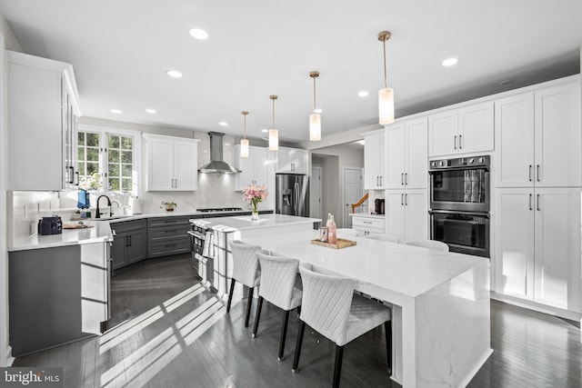 kitchen with multiple ovens, a kitchen island, white cabinetry, stainless steel fridge, and wall chimney exhaust hood