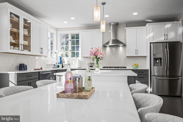 kitchen with a kitchen bar, backsplash, stainless steel appliances, wall chimney range hood, and glass insert cabinets