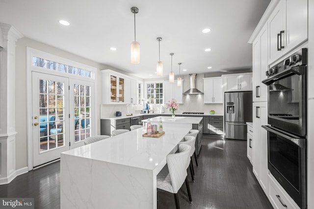 kitchen with dark wood-style floors, a kitchen island, stainless steel appliances, and wall chimney range hood