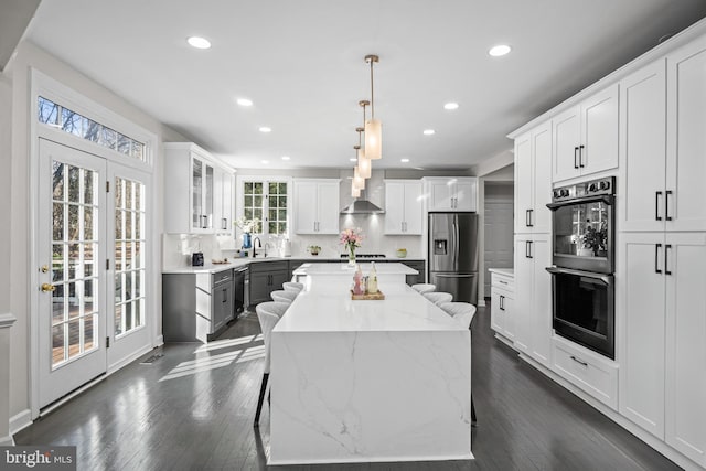 kitchen with a kitchen island, stainless steel fridge with ice dispenser, white cabinetry, double oven, and wall chimney range hood