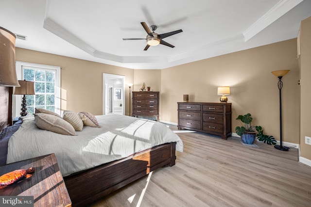 bedroom with light wood-type flooring, visible vents, a tray ceiling, baseboards, and ceiling fan