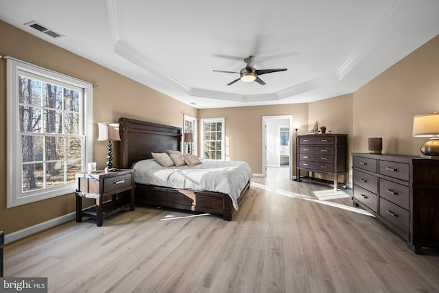 bedroom with light wood finished floors, visible vents, baseboards, and a tray ceiling